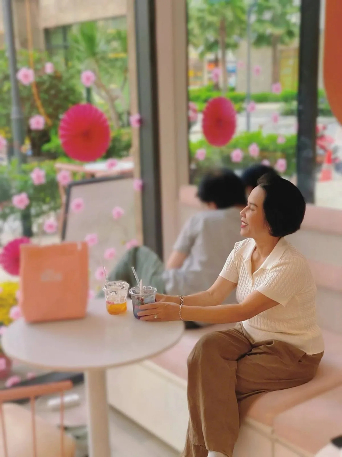 Khách ngồi trong quán The Hoa Grand Park bên ly trà và túi giấy hồng