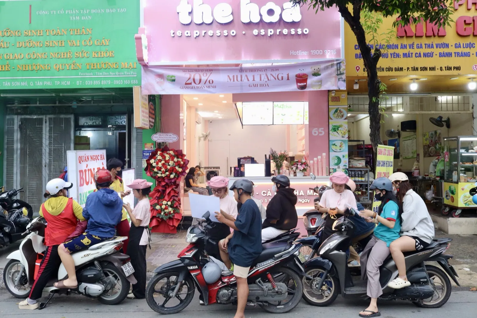 Khách đi xe máy và nhân viên trước mặt tiền màu hồng của The Hoa Tân Phú dịp khai trương